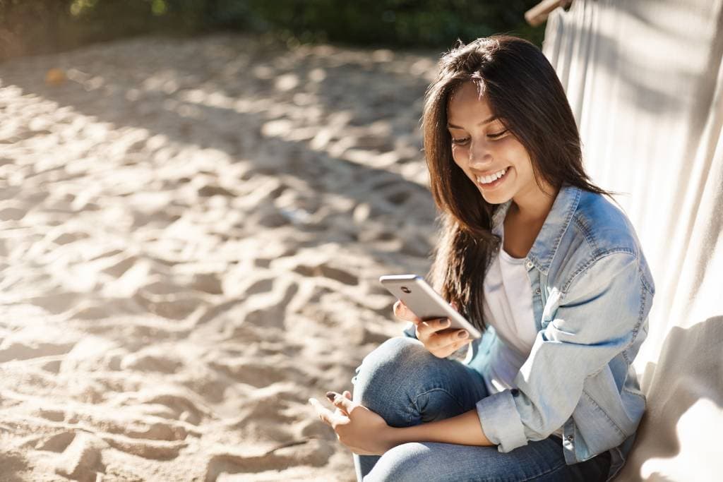Woman sitting on the beach on her phone